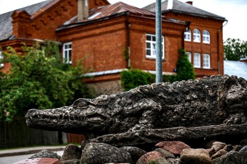 Crocodile sculpture in front of a historic brick building in green surroundings, Dundaga, Latvia
