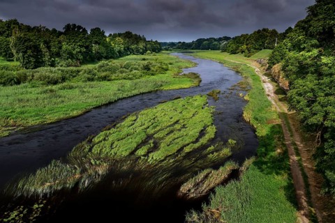 Musa river with green surroundings under cloudy sky, Bauska, Latvia