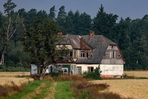 Abandoned house surrounded by fields and trees under cloudy sky, Zemgale, Latvia