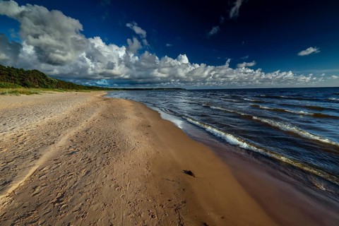 Vastness of Vitrupe beach with thick clouds and rolling waves under clear skies, Vitrupe, Latvia