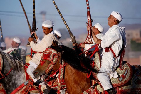 Group of riders wearing traditional clothing hold up rifles at a historic Fantasia event, El Kelâa
