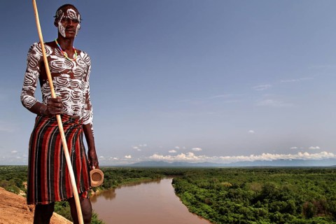 Man wearing traditional clothing looks at a river in Murle village, Murle, Ethiopia