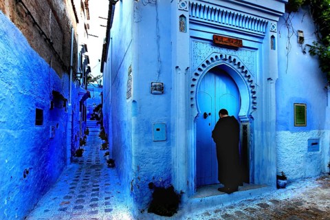 Blue alley with traditional Moroccan gate and a person in the medina of Chefchaouen, Chefchaouen,