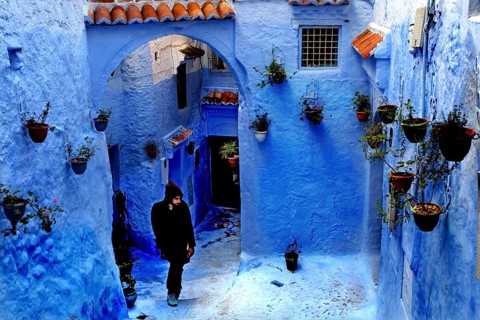 Blue alley with arches and flower pots interspersed with a passing person in the Medina,
