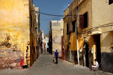 Sunlit narrow alley with passer-by and old buildings, El Jadida, Cité Portugaise, Morocco