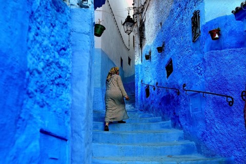 Woman in traditional dress climbing the blue steps of a Medina alley in Chefchaouen, Chefchaouen,