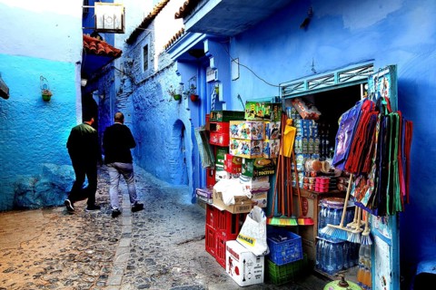 Market stand on a blue wall in the medina of Chefchaouen, people strolling, Chefchaouen, Morocco