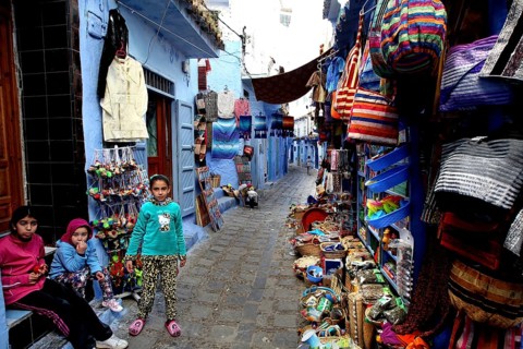 Alley in the medina of Chefchaouen with colorful goods and children playing, Chefchaouen, Morocco