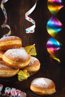 A pile of donuts with powdered sugar, colorful garlands and streamers against a dark wooden
