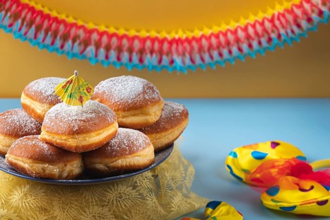 A plate of donuts with powdered sugar on a table surrounded by colorful carnival decoration