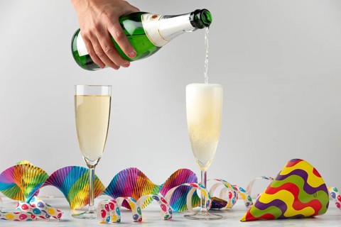 Sparkling wine is filled into glasses surrounded by colorful streamers, carnival