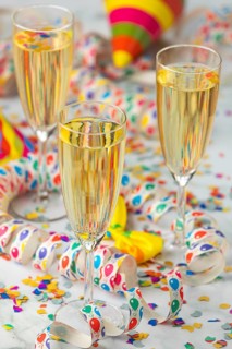 Three champagne glasses with colorful hats and confetti on a table, carnival