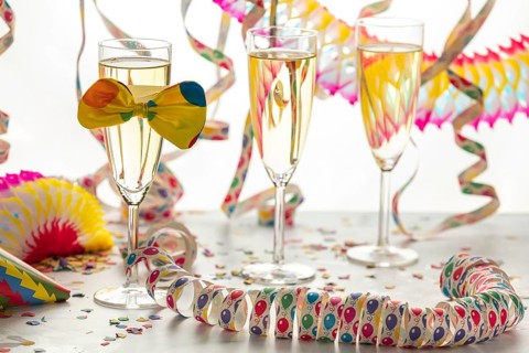 Three champagne glasses decorated with bows, surrounded by colorful confetti and streamers,