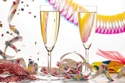 Two filled champagne glasses with colorful streamers, mask and confetti, carnival