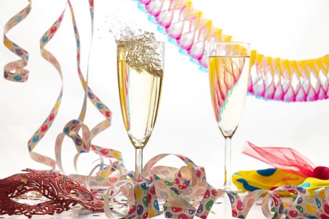 Two champagne glasses, one sparkling, in a lively atmosphere with streamers and a mask, carnival