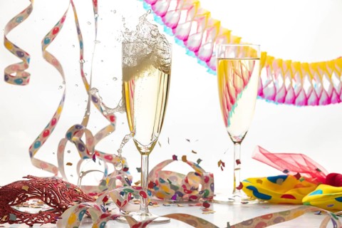 Two champagne glasses, one sparkling, in a lively atmosphere with streamers, confetti and mask,