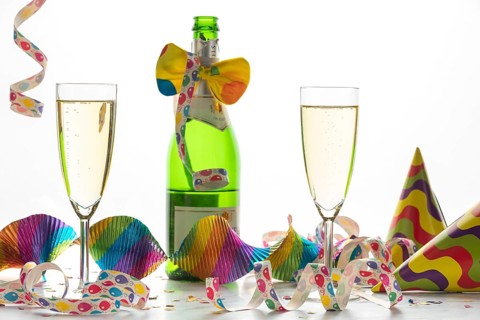 Two champagne glasses and a bottle surrounded by colorful streamers and hats, festive atmosphere,