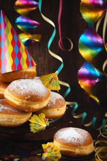 A pile of donuts with powdered sugar, colorful garlands and party hat against a dark wooden