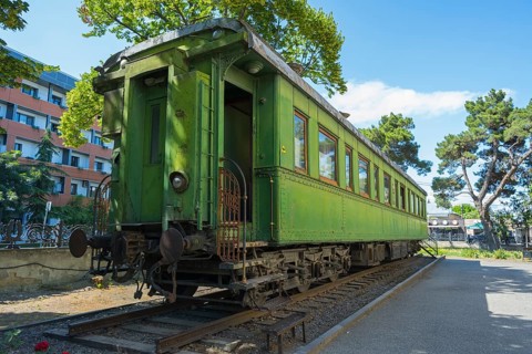 Green historic train car on rails between trees in an urban environment, Stalin's personal railroad
