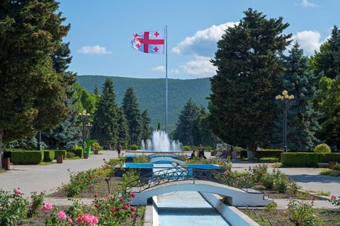 Parkland with central fountain surrounded by flowers and tall trees, Georgian flag, Stalin Park,