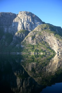 Majestic rocks reflected in clear water under a bright blue sky at Lysefjord, Rogaland, Norway