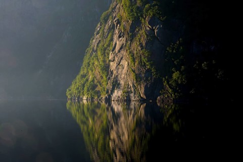 A steep rock rises up, its massive presence reflected in still water, Lysefjord, Rogaland, Norway
