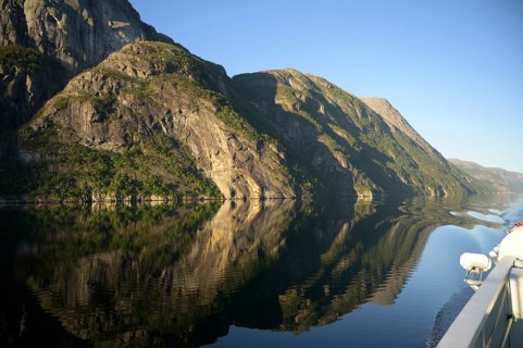 A boat sails along an orderly and peaceful Lysefjord surrounded by massive rock walls, Lysefjord,