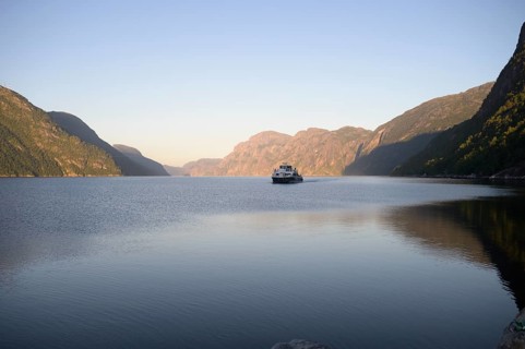 Columbus shipping company ferry in the middle of the quiet Lysefjord at dusk surrounded by