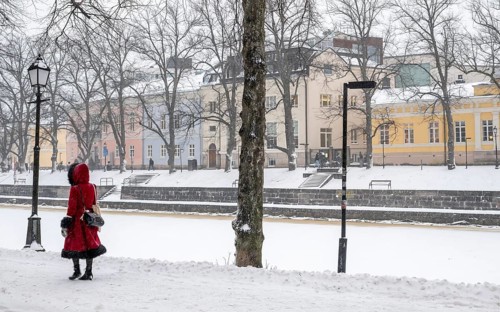 Woman in red winter coat walks along the frozen Aurajoki river, wintery Turku or Swedish Åbo,