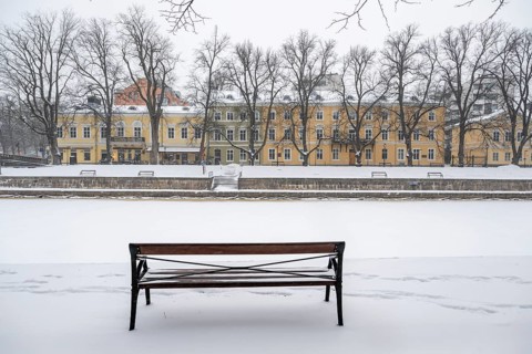 Bench and historic buildings on the frozen Aurajoki river, wintery Turku or Swedish Åbo,