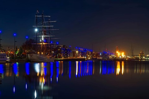 Nocturnal harbor with illuminated sailing ship and reflections in calm water