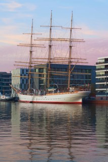 Large sailing ship in harbor in front of modern buildings at dusk