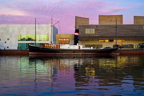 Harbour with illuminated tugboat and evening sky in shades of pink and blue