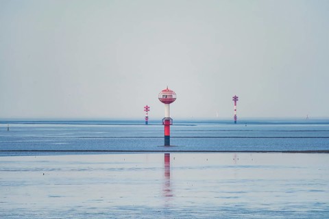 A red and white water buoy in the vast blue sea under a bright sky