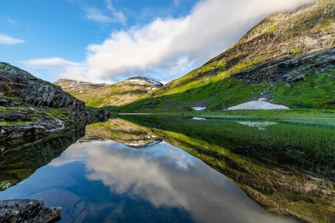 Mountains with snow-capped peaks reflected in clear water surrounded by green vegetation