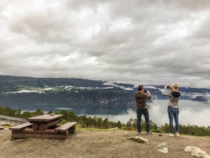 Utvik, Vestland, Norway, Two people taking pictures of a misty mountain backdrop with a lake in the