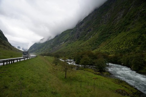 Byrkjelo, Vestland, Norway, truck on road in valley with towering mountains and a river next to it