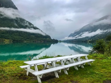 Olden, Vestland, Norway, white picnic table at a lake with mountains and low-hanging clouds in the