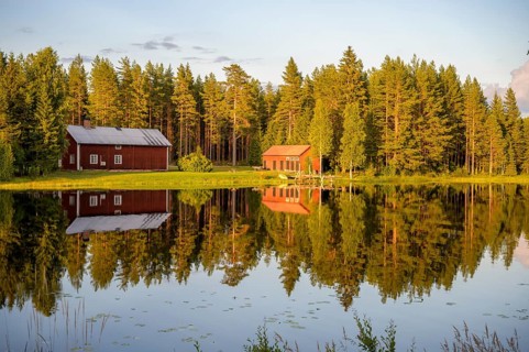 Östanå, Torsby, Värmland, Sweden, Two red buildings by the lake, perfectly reflected in calm water,