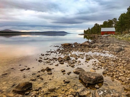 Drevsjø, Innlandet, Norway, The quiet Femund Lake with stones in the foreground and a red house in