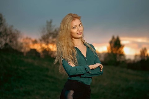 Cheerful woman with blonde hair stands with her arms crossed on a heel during sunset. Retreat in a