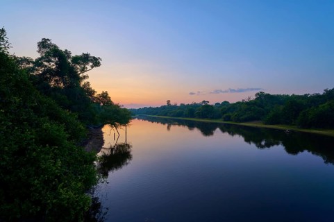 A quiet river morning with shades of blue and orange at sunrise, trees on the shore, Fazenda