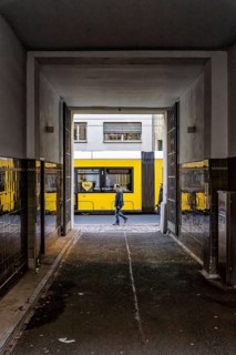 View through a corridor to the backyard onto Chässeestraße with passengers and moving tram, Berlin,