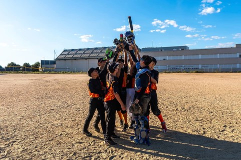 Young baseball players huddling together with arms raised in victory, holding bats, gloves, and