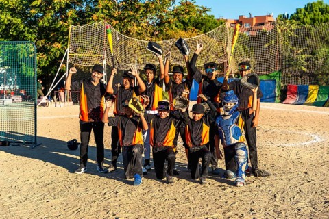 Young baseball team and coach standing together on an outdoor dirt field, raising bats and gloves