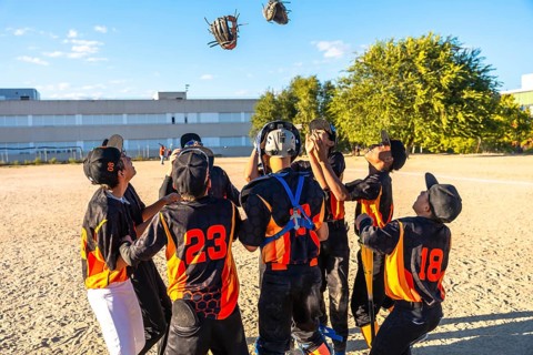 Young baseball players with gloves and uniforms celebrating a game victory together on a dirt