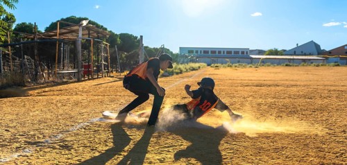 Two baseball players on a sunny field, one slides into a dusty base in a cloud of dirt while