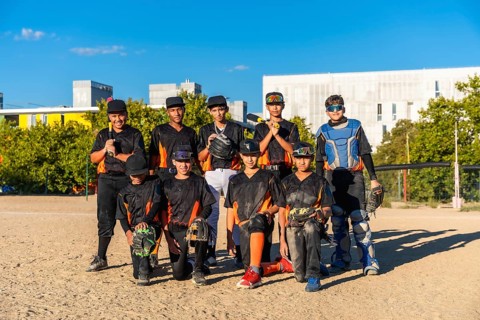 Young baseball players wearing uniforms and protective gear on a sunny day, standing and kneeling