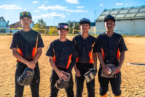 Young baseball teammates in uniforms posing with mitts and a ball on a dusty sunlit field, ready