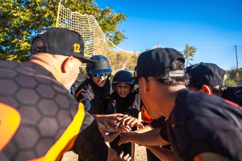Baseball coach and diverse youth team link hands in a motivating pre game huddle on a sunny field,